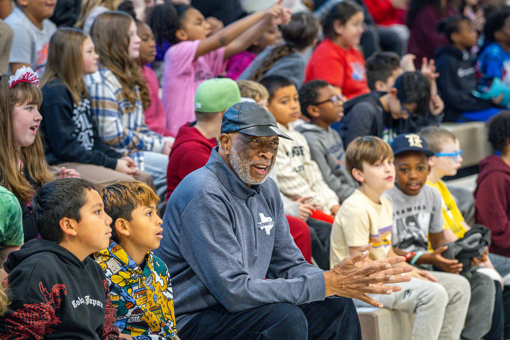 Jagours smiling and clapping as he sits among students in the gym bleachers