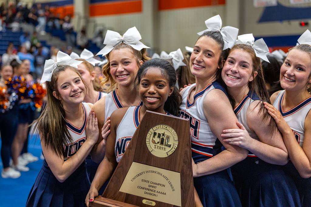members of the cheer team gathered around cheerleader holding state champion trophy