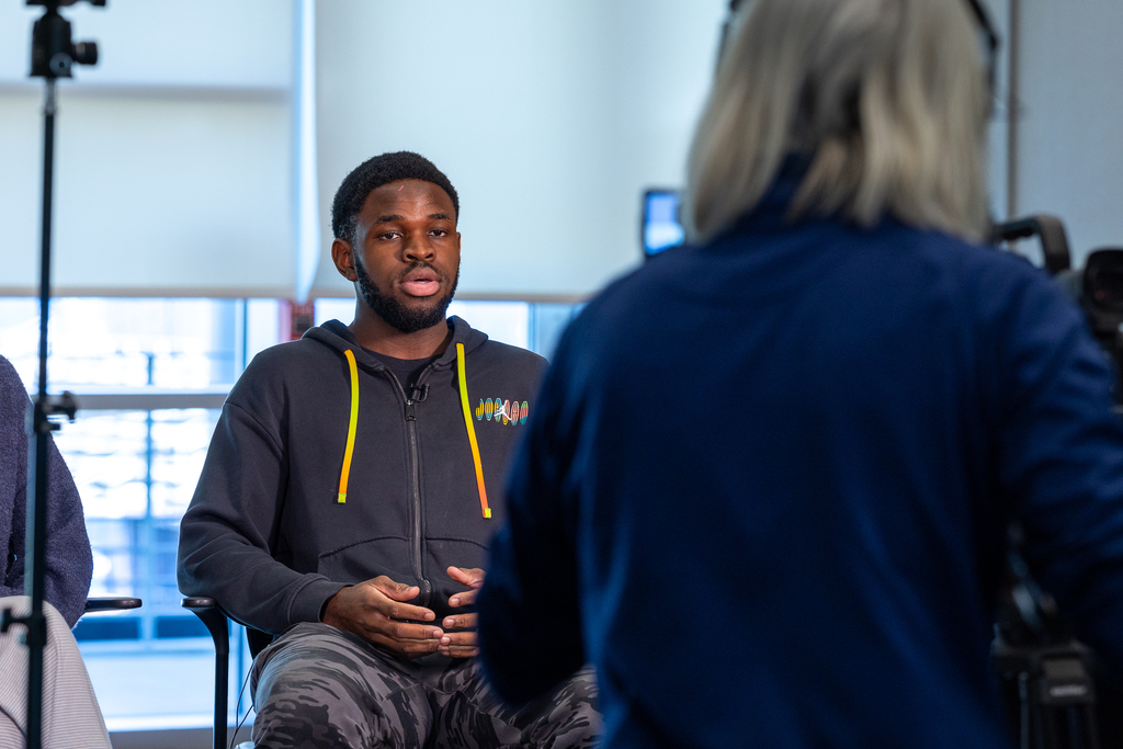 male student sitting on stool talking on camera 