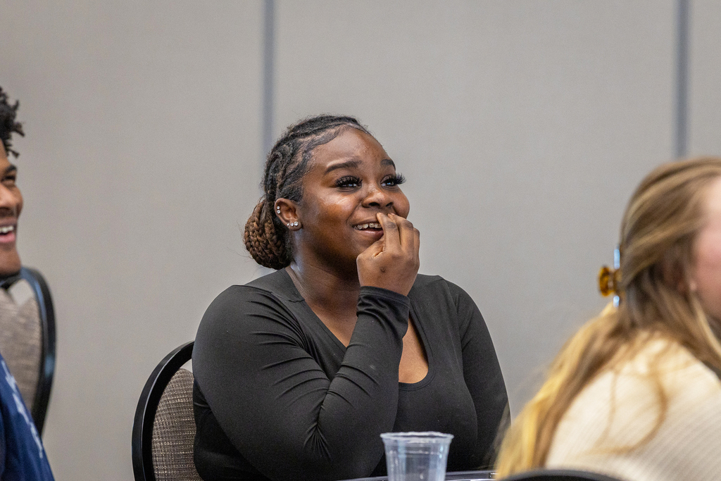 female student with her hand covering her mouth as she looks up at screen and laughs