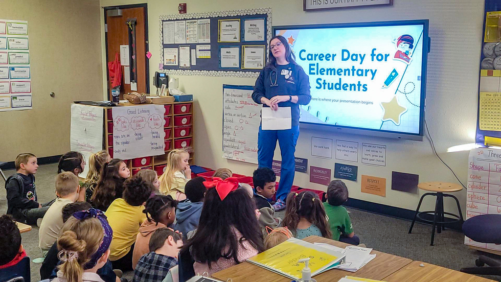 woman in nurse attire talking to group of students seated on the floor