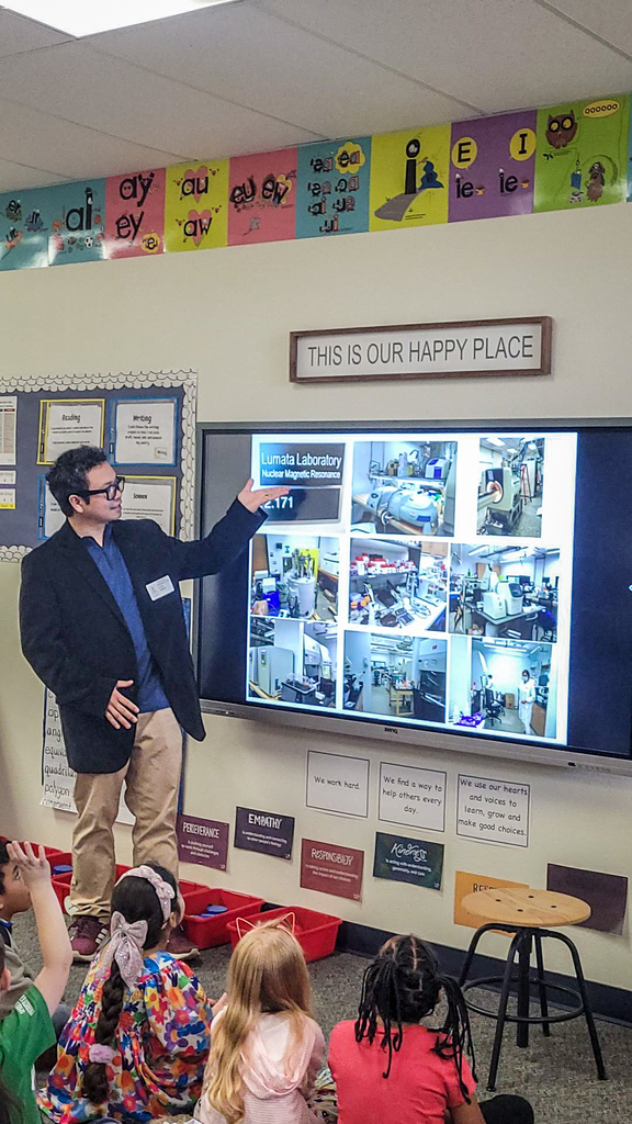 man pointing to photos on display screen in front of class as he talks about his job