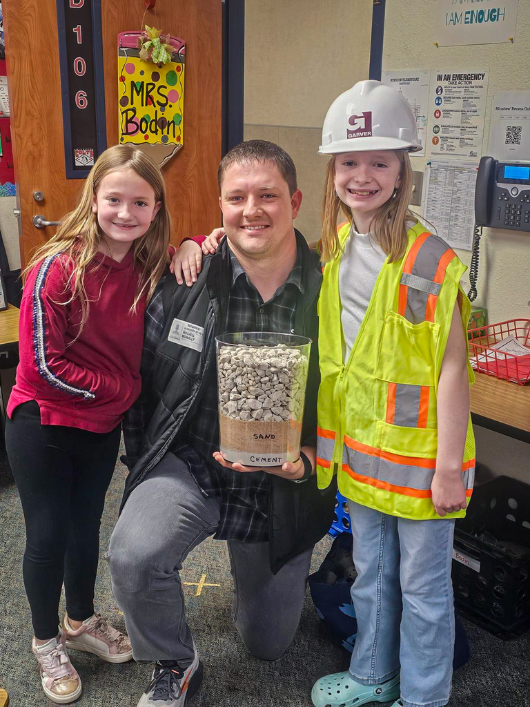 man kneeling next to two girls and one is wearing a construction hard hat and safety vest
