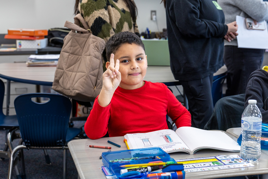 male student holding up peace sign gesture as guests stand behind him