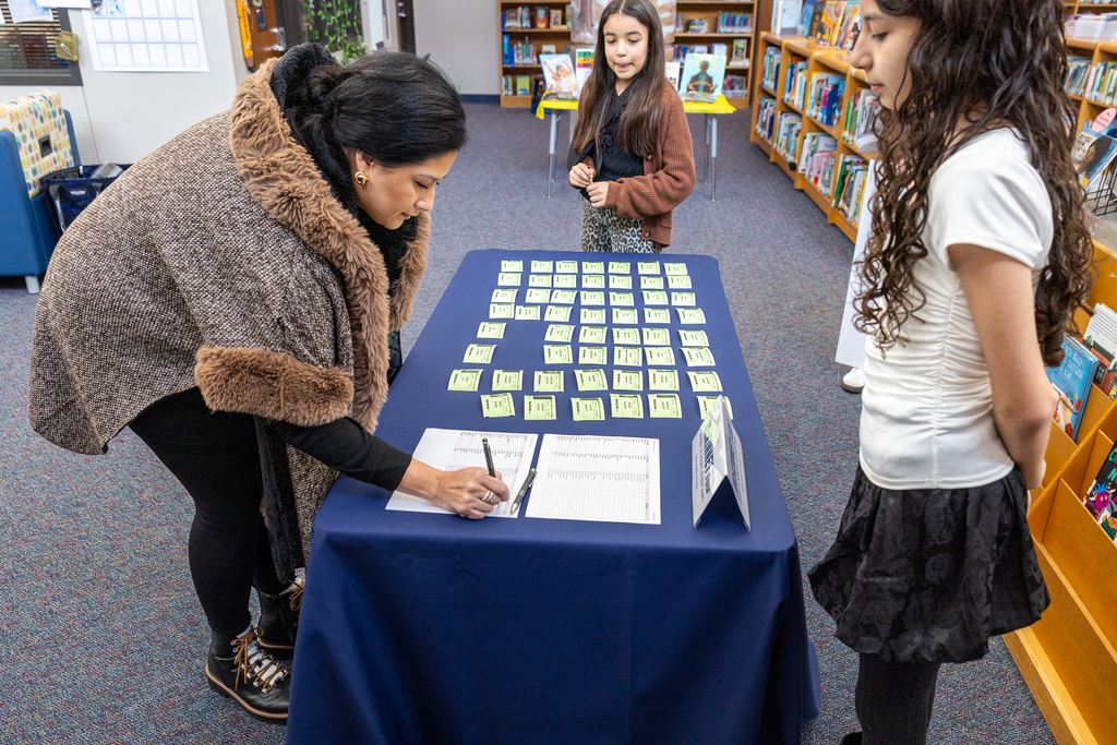 woman signing it at table as student greeters look on