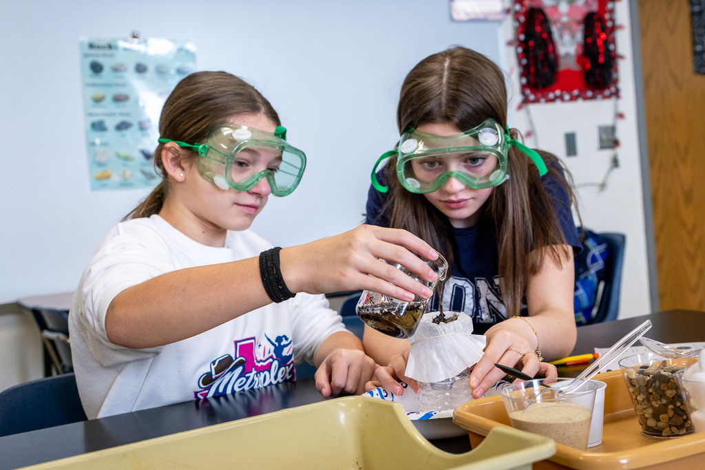 two female students in lab goggles working on project