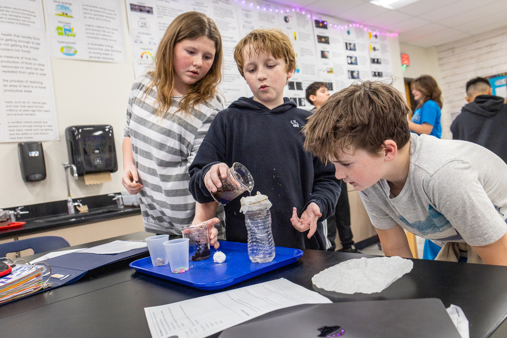 female student and two male students working in a group and looking as one male student pours solution into filter on bottle