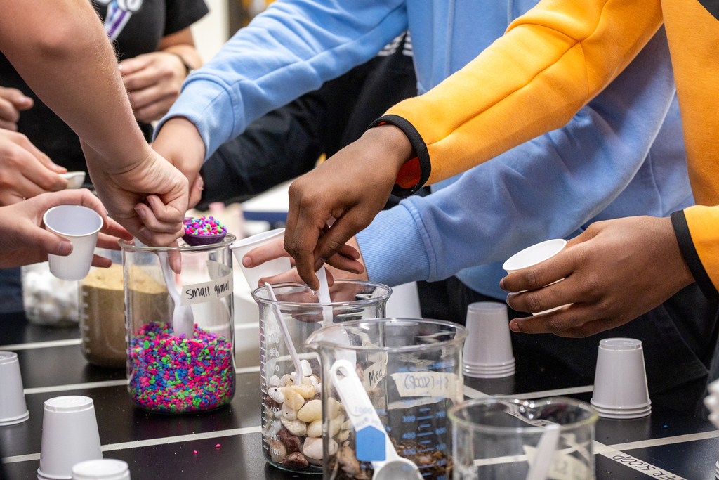 students hands reaching to get materials for the water filtration lab