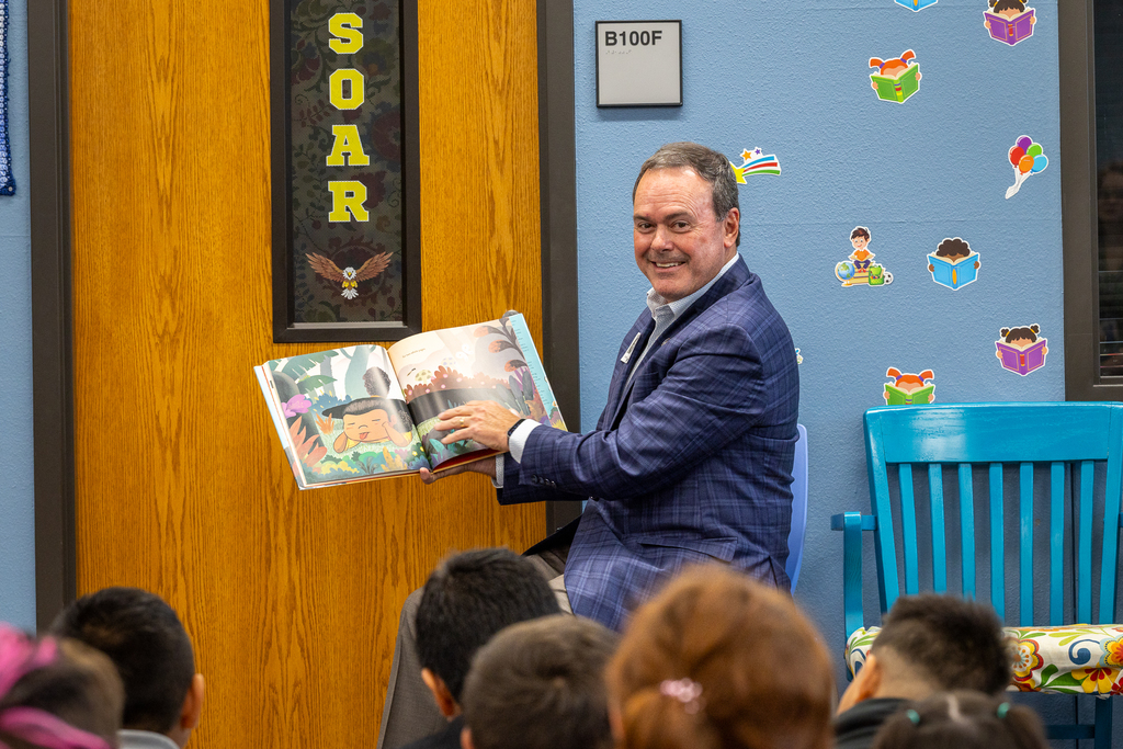 Cox seated with book smiling at audience