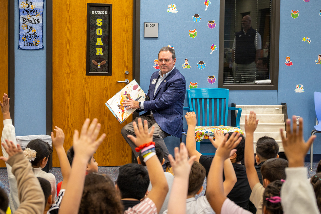 Cox seated with book and hands raised in the crowd