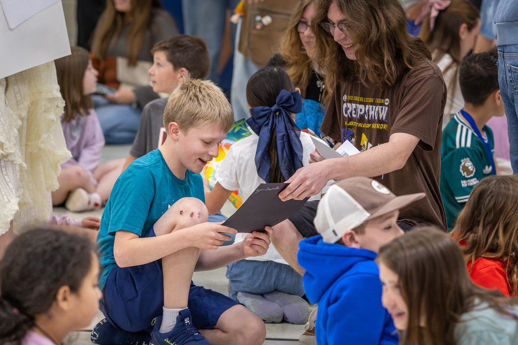 male 3rd grader reacting with a smile as high schooler hands him the finished art piece