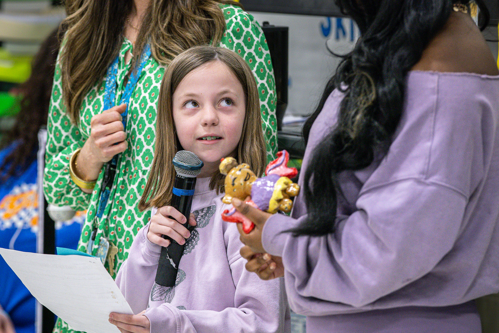 female third grade student holding microphone looking up at female high school student who is holding her sculpture of the project