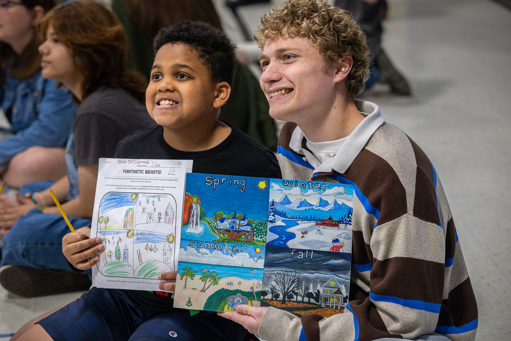 male third grade student and male high school student smile as they hold up their versions of the project