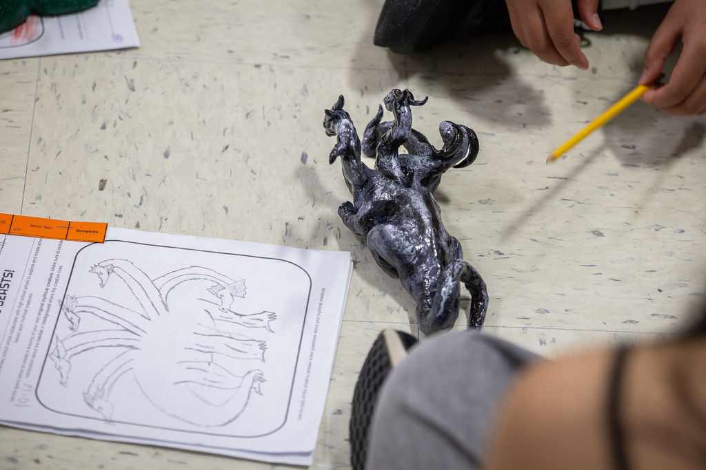 detailed sculpture of multi headed dragon at the feet of 3rd grader and high schooler next to 3rd grader's idea sketch