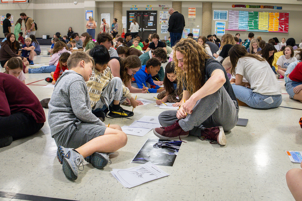 male high school student working on a drawing activity with two male 3rd grade students