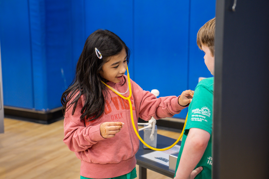 girl using toy stethoscope on classmate