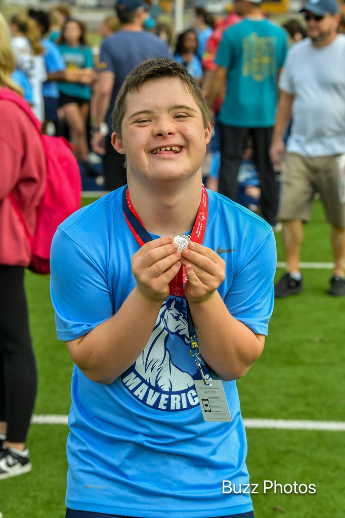 male competitor holding up medal and smiling widely at the camera