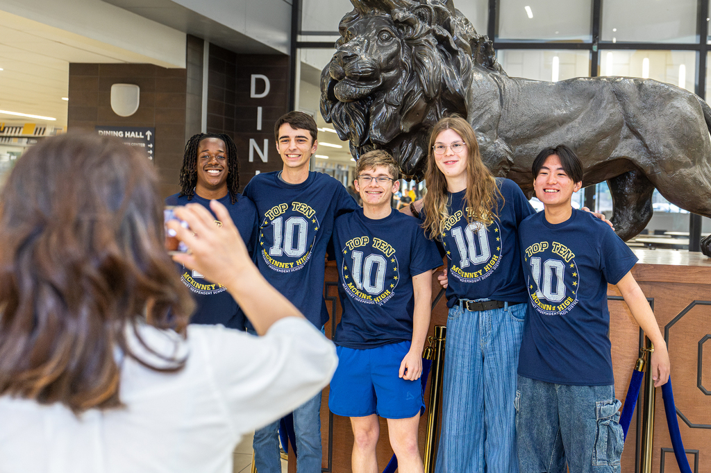 group of top 10 students in front of lion statue as mom takes a photo