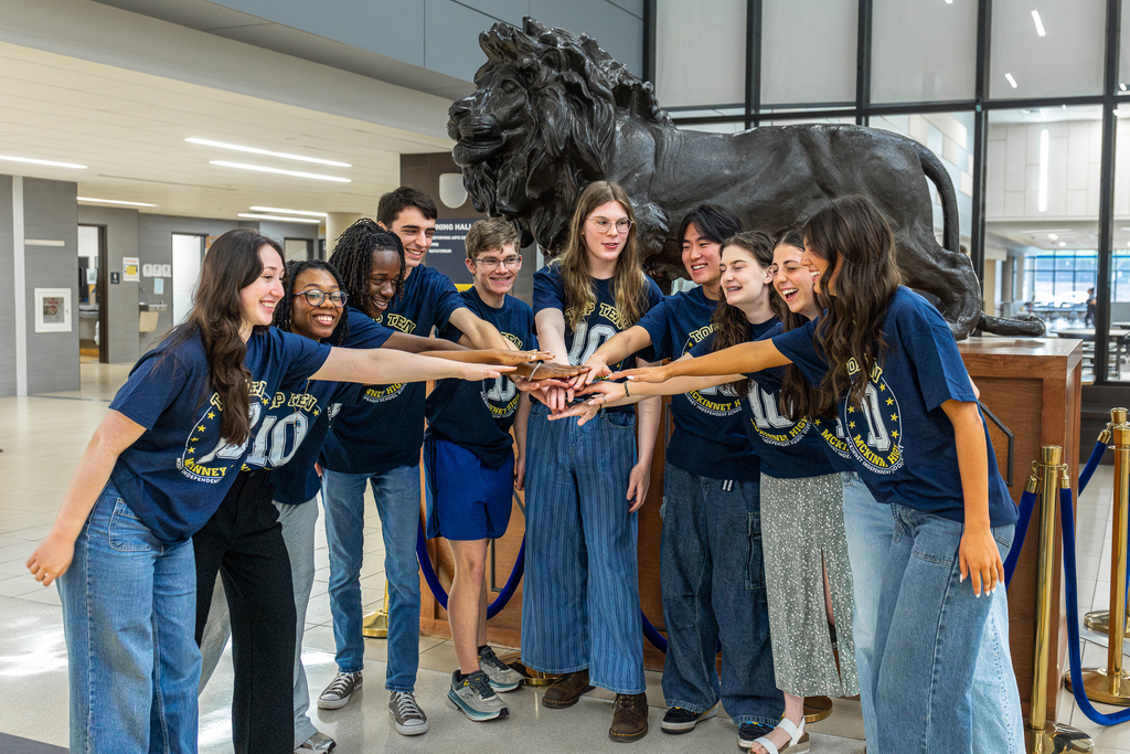 top 10 students in front of lion statue in a circle with hands in 