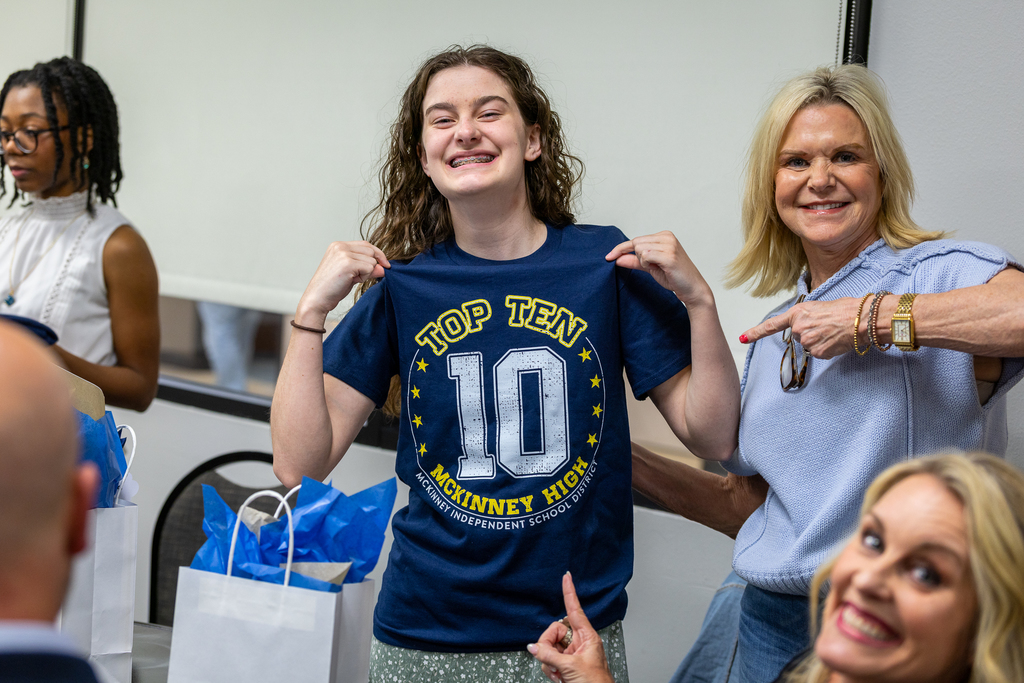 #9 student Saylor Baker smiling and pointing at top 10 shirt as mom and administrator point at it 
