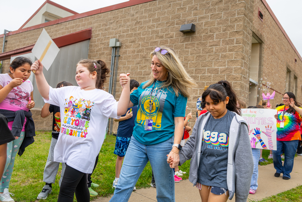 Wendy Cottam holding the hands of two of her students as they walk in the parade