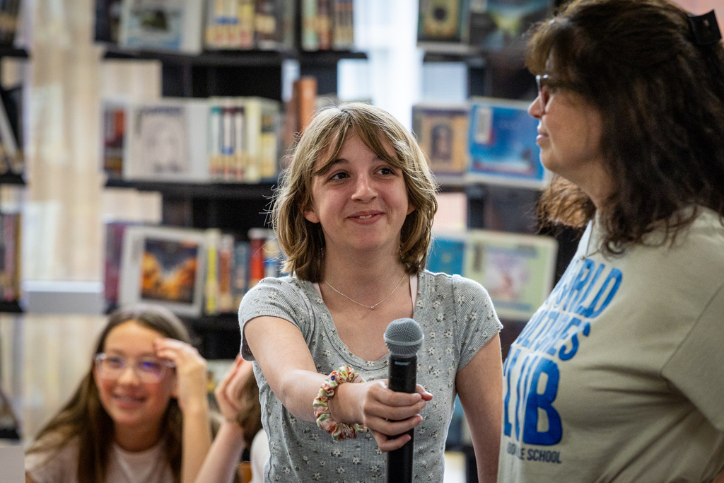 girl laughing and handing microphone back to teacher
