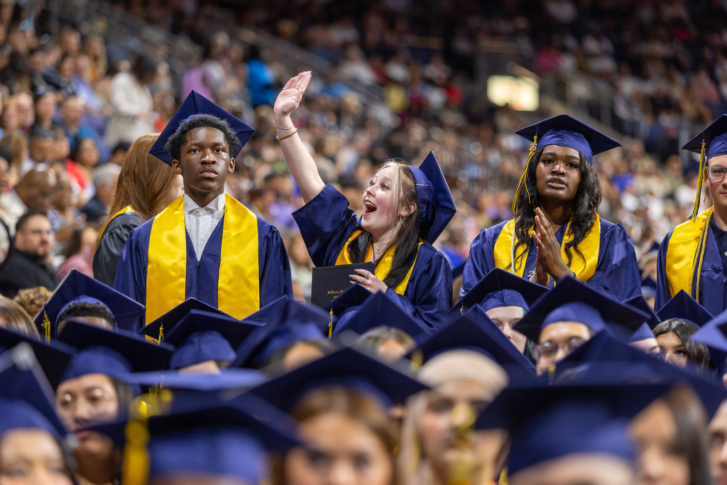 female graduate waving excitedly to someone in the audience 