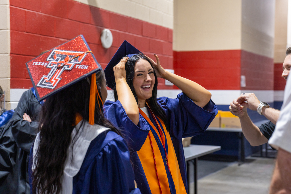 female graduate backstage laughing and adjusting cap