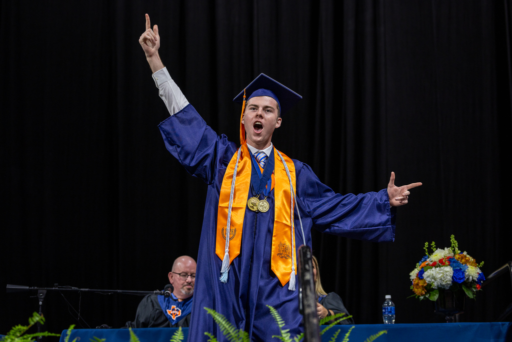 male graduate onstage making bold celebratory gesture