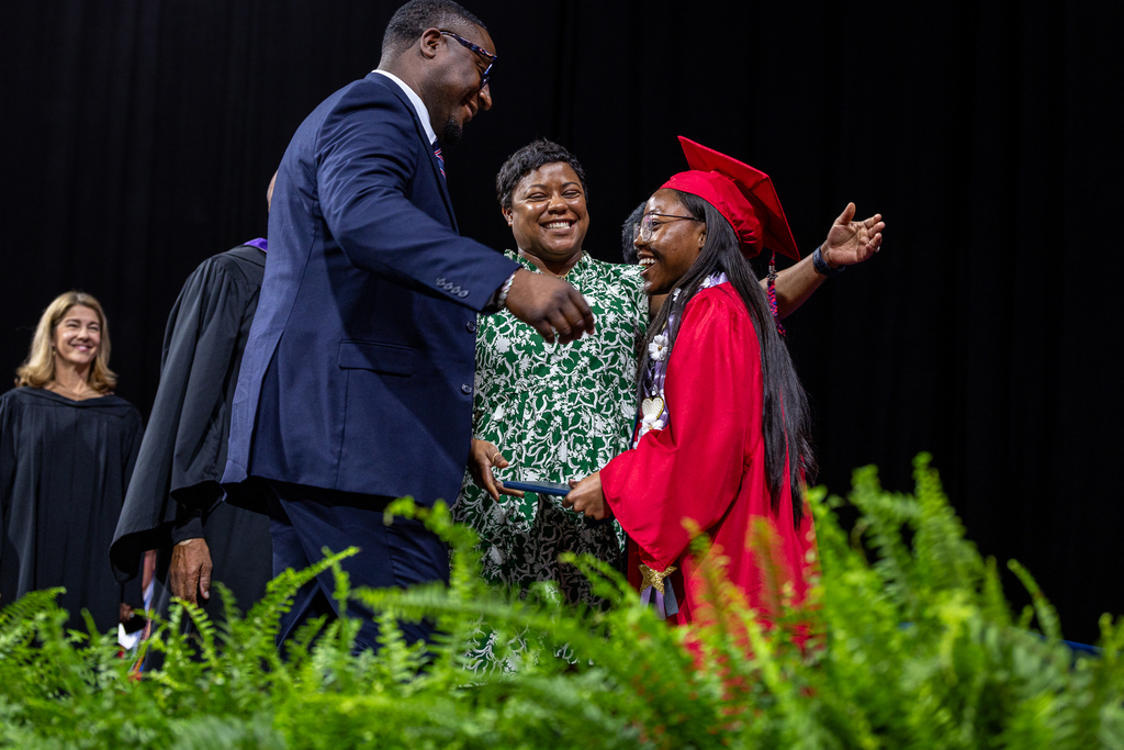 teacher parents onstage with graduate smiling and embracing her
