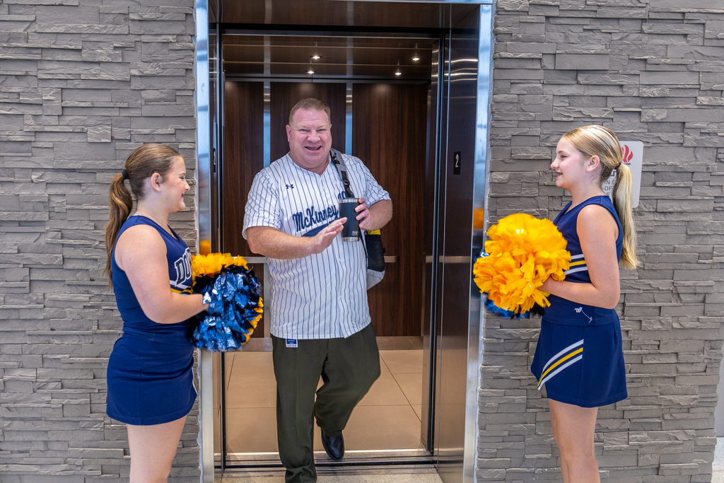 administrator getting off elevator with cheerleaders greeting him