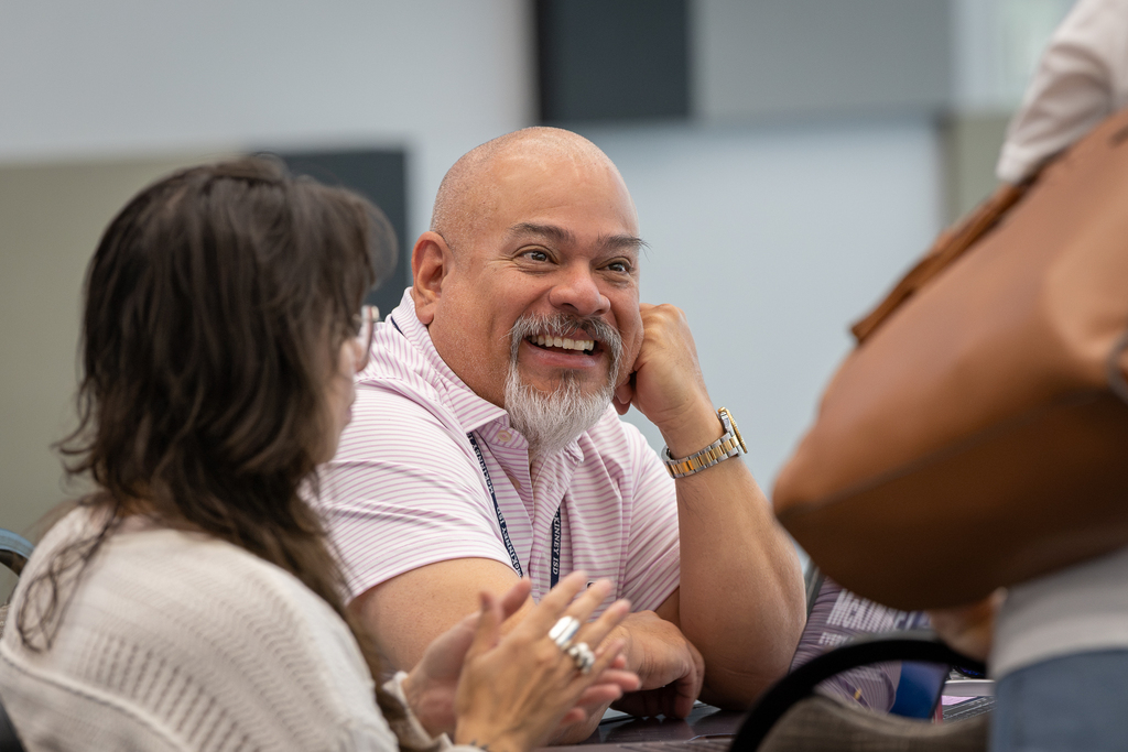 male teacher smiling at table as he talks with colleagues