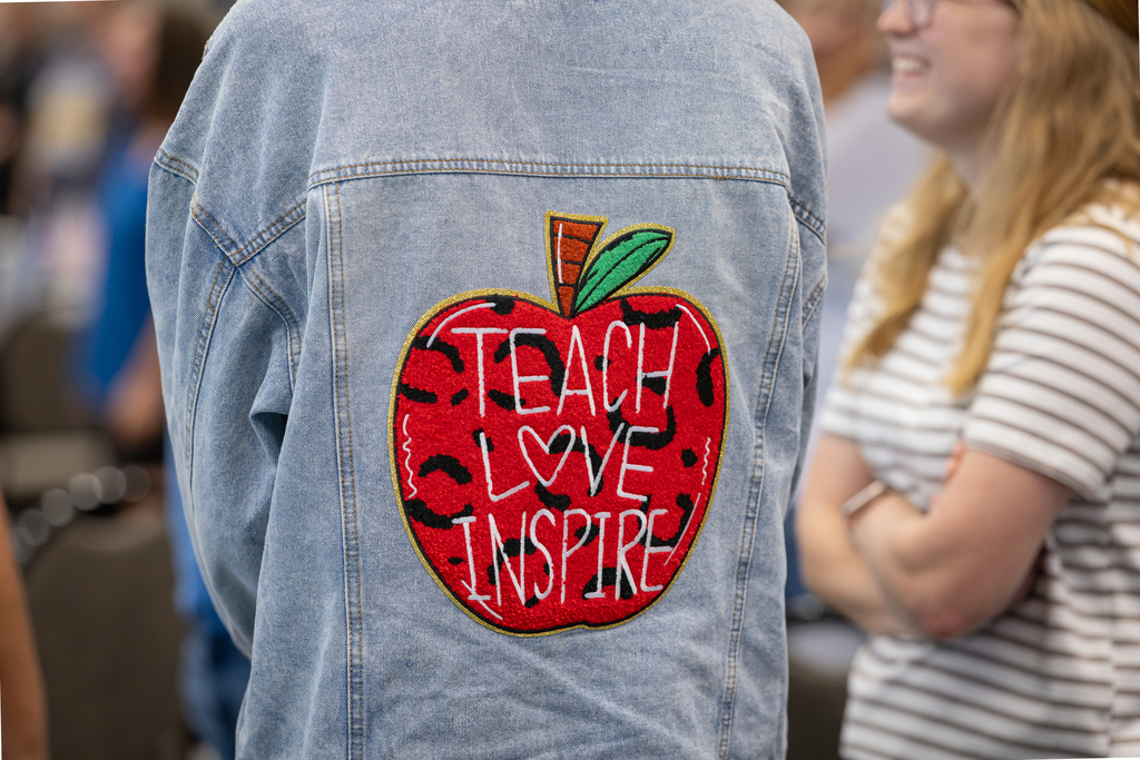 teacher with jacket on that reads "teach, love, inspire"