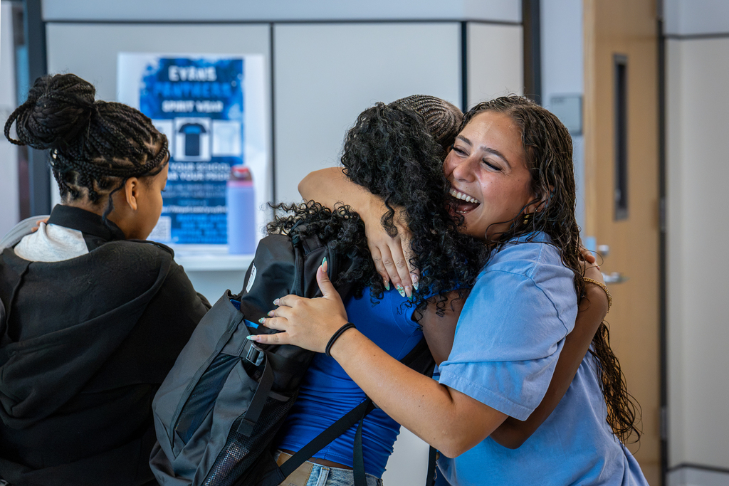 female teacher greeting a female student with a big hug and smile