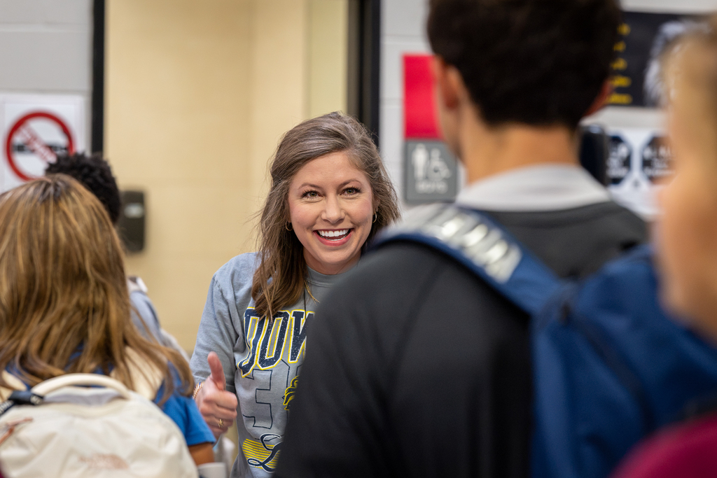 female teacher smiling at students as they enter the building