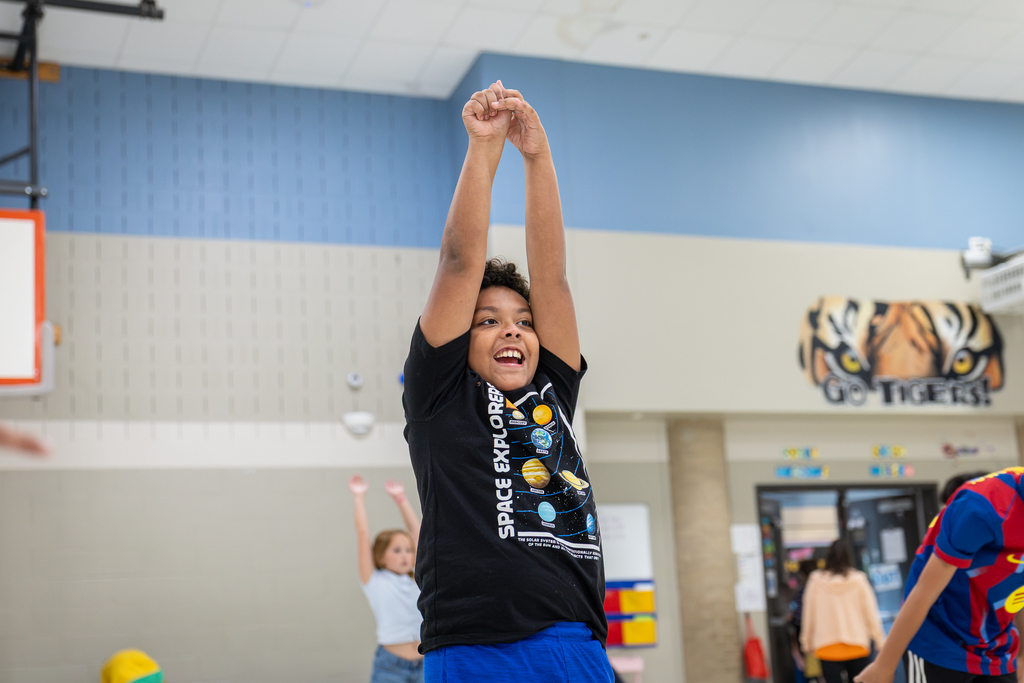 boy in gym smiling and doing stretching with hands up over head