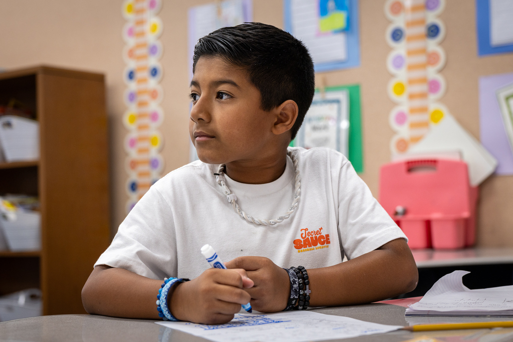 boy at desk with marker looking toward teacher