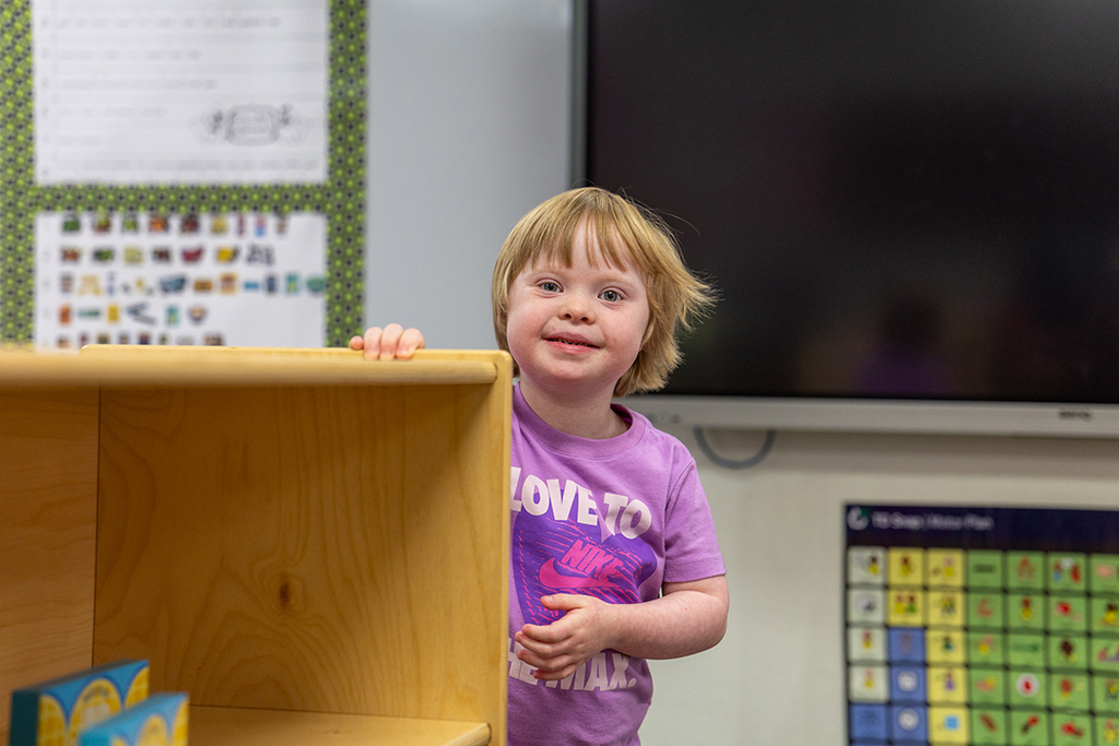 girl looking around corner of bookshelf smiling at camera