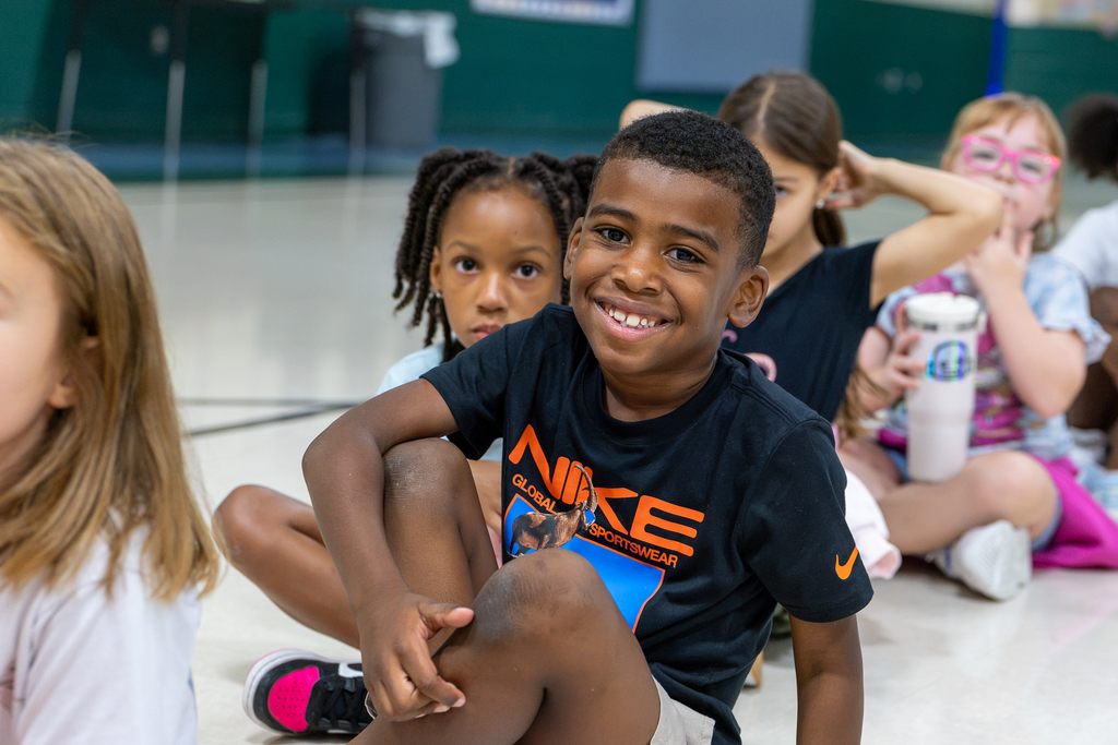 male student smiling at camera as he sits in the gym with other students