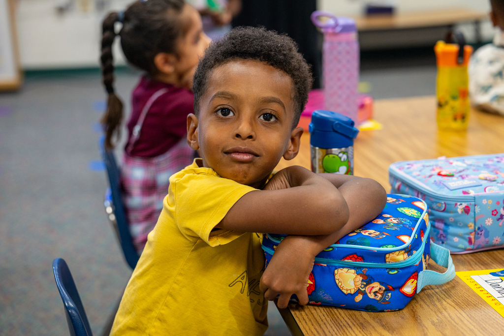 male student looking at camera as he waits with his lunch at his desk