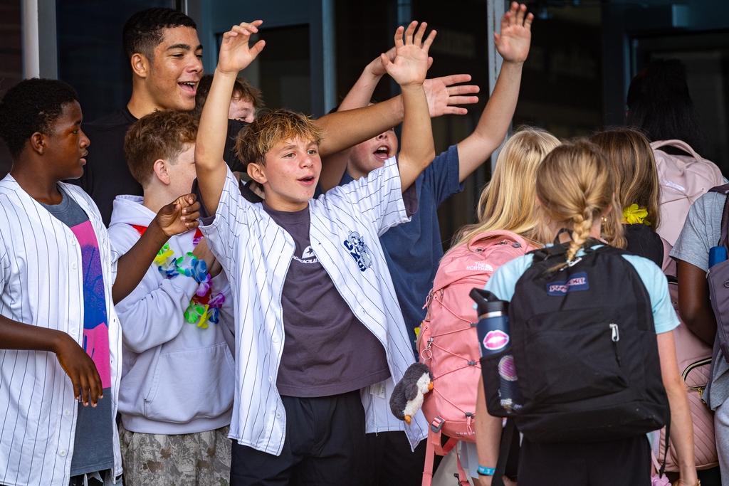 boys with arms in the air greeting students as they enter the building