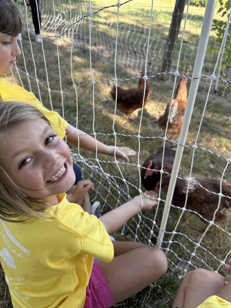 One student smiling up at camera while feeding a chicken