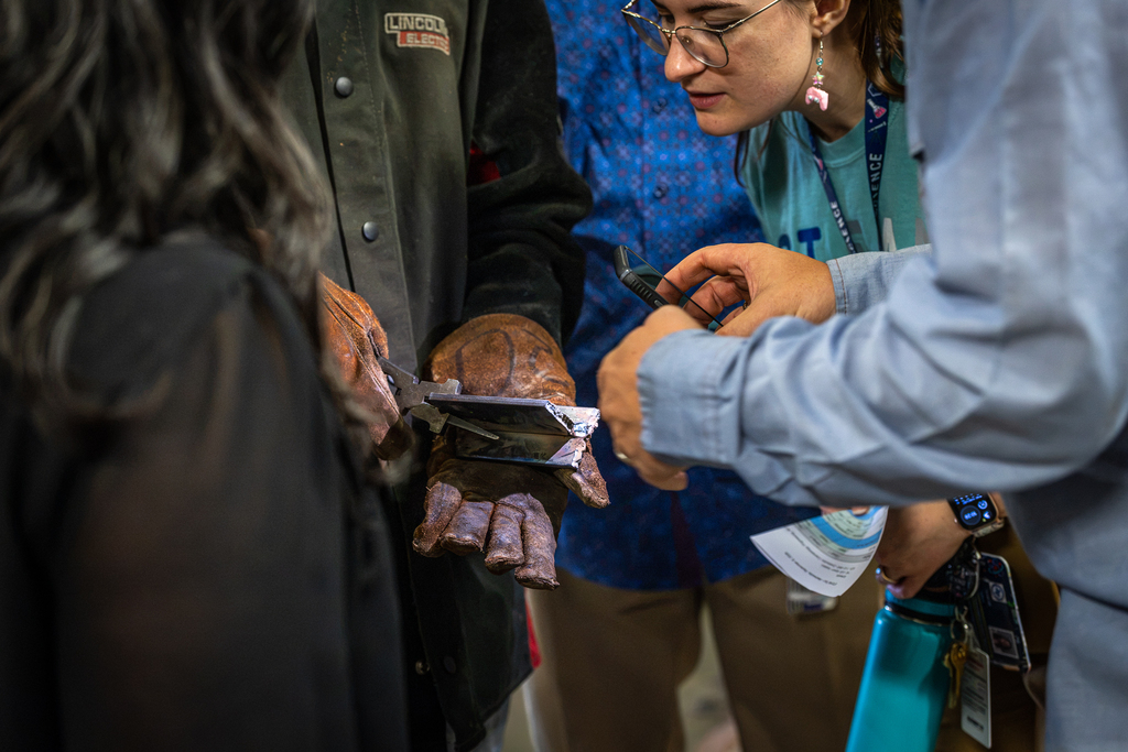 teacher peering in to look closely at a welded piece of metal held by student