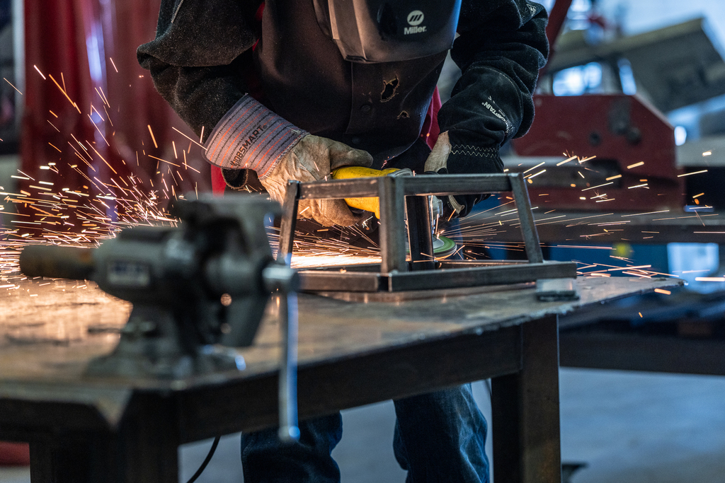 sparks flying as student in protective gear grinds the edges of a metal part he is fabricating