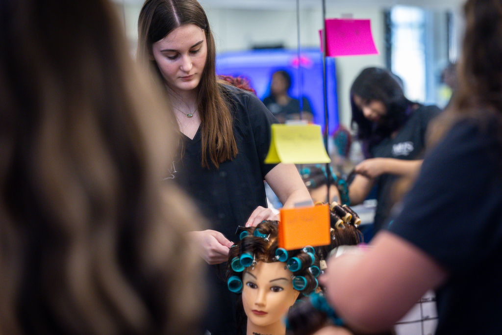 reflection of female cosmetology student working on a manaquin hairstyle