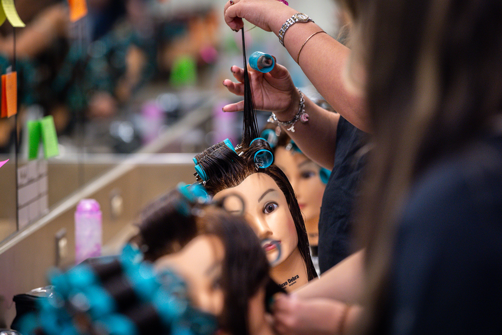 hands putting rollers in hair of instructional mannequin head