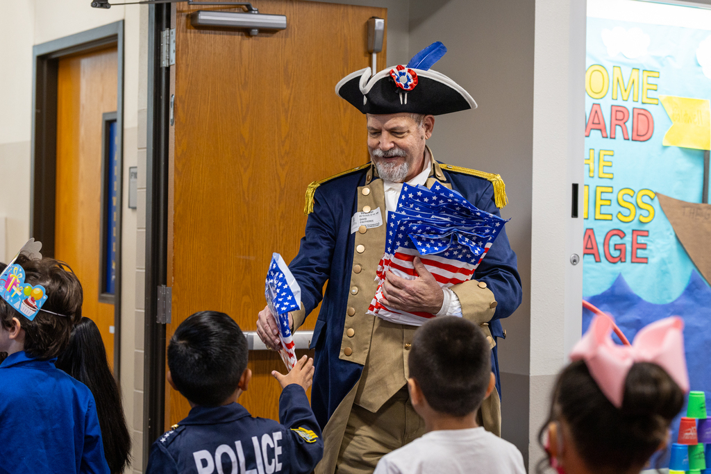 man in colonial clothing handing patriotically colored bags to students in line