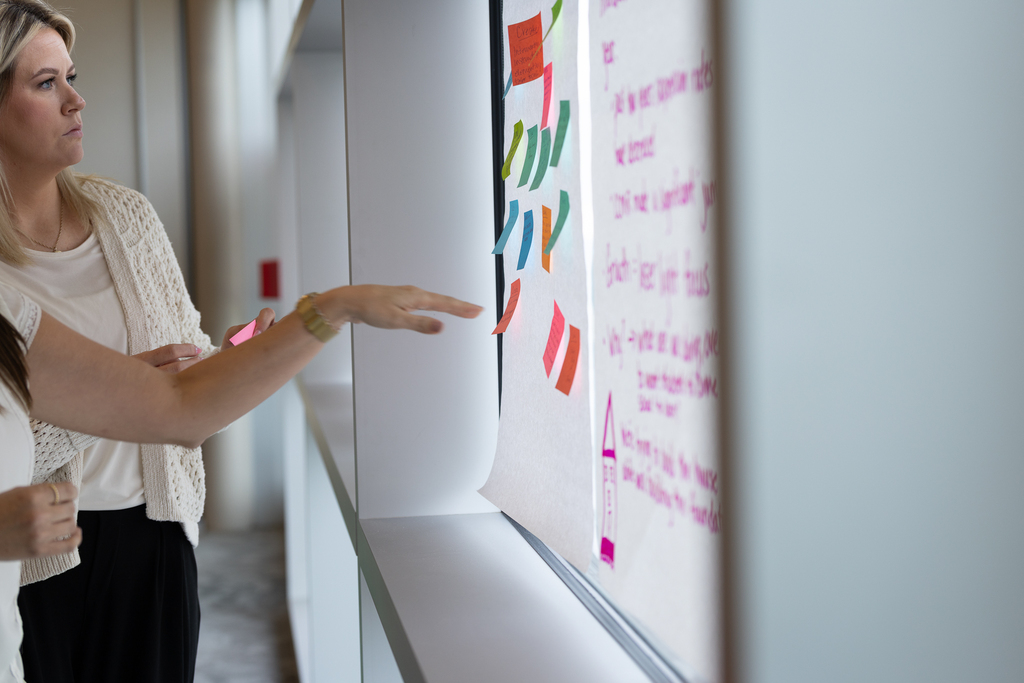 two women placing post it notes on collaborative poster paper
