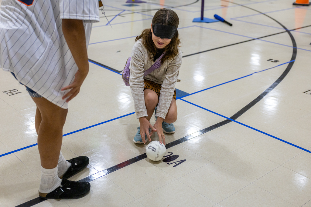 girl with a blindfold on trying to follow voice directions to locate and pick up a ball