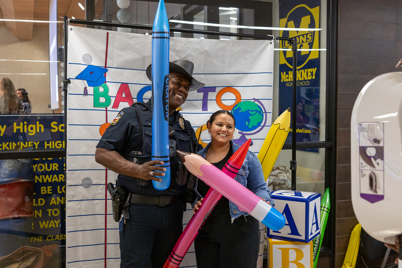 SRO and teacher in photo booth holding inflated pencils and crayons